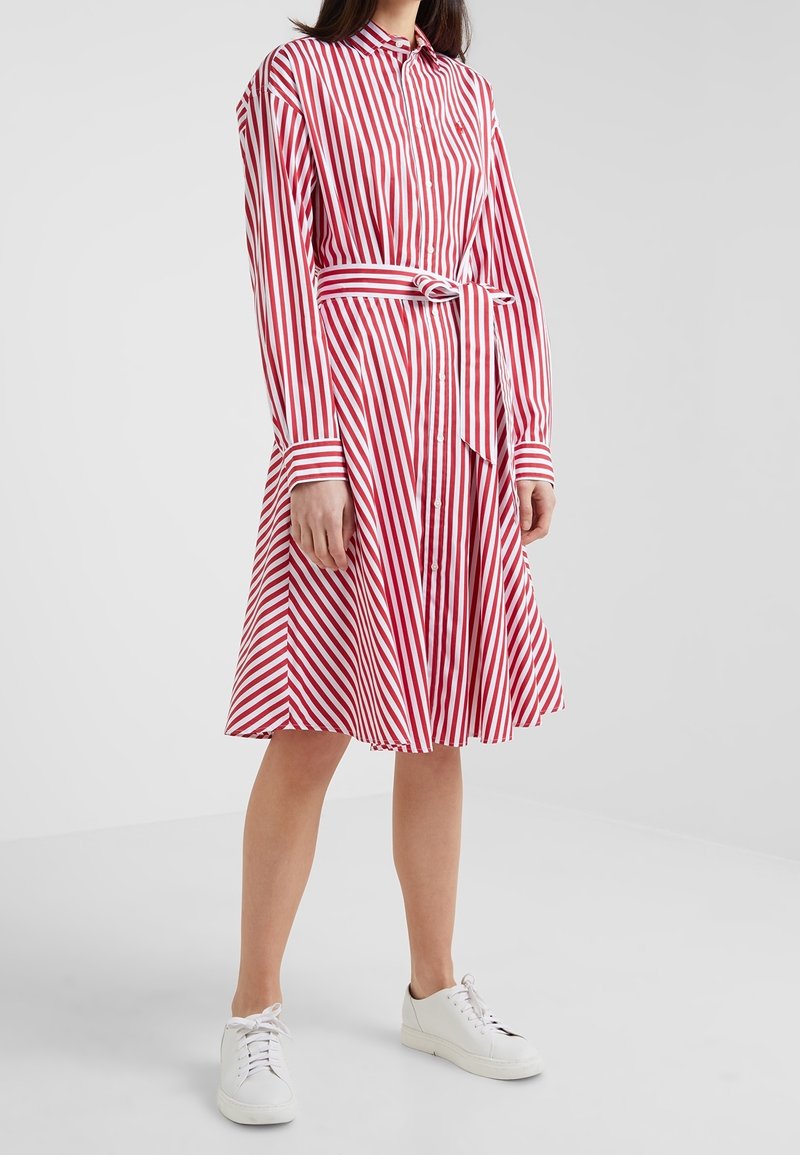 Czerwona i biała sukienka w paski z kołnierzykiem, długimi rękawami, z przodu na guziki, z wcięciem w talii z materiałowym paskiem i plisowanym dołem.