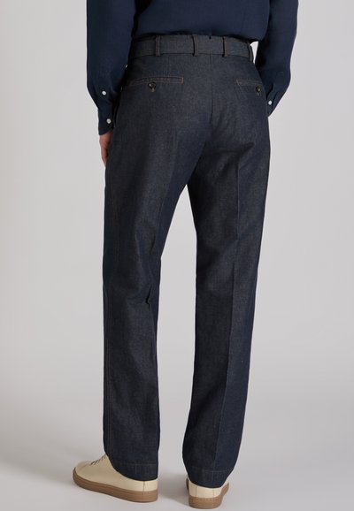 Dark blue denim trousers with a straight fit, featuring back pockets and contrasting stitching. Worn with cream-colored sneakers.