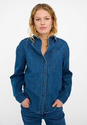 Niebieska koszula dżinsowa na guziki z długimi rękawami, pojedynczą kieszenią na piersi i standardowym kołnierzykiem. Charakteryzuje się ciemnymi guzikami i luźnym krojem.