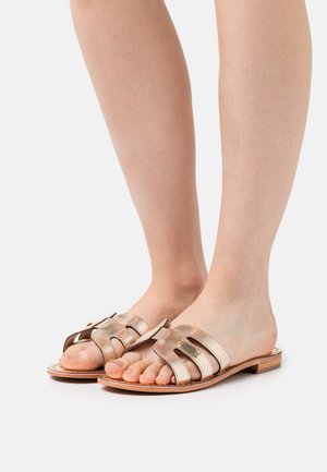 Sandali in pelle dorata con suola piatta, dotati di cinturini larghi e design forato per la ventilazione. La finitura è leggermente lucida e liscia.