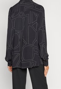 Maglietta nera a maniche lunghe con cuciture geometriche bianche. Presenta una vestibilità comoda e polsini con bottone. Realizzata in un tessuto liscio.