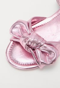 Rosa metallisk sandal med en rosett på remmen. Slät yta, rund tådesign och mjukt innerskikt.