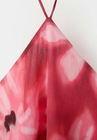 Tissu tie-dye rouge et rose avec de fines lignes verticales formant une forme triangulaire, maintenu par deux fines bretelles rouges en haut.