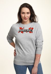 Felpa grigia con logo pixelato di "Minecraft" e cuori rossi. Maniche lunghe e polsini a coste con una vestibilità rilassata.