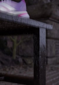 Pink and white sneaker on the edge of a dark wooden bench with blurred outdoor background.