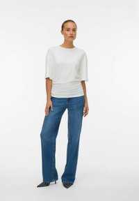 Haut blanc à manches courtes avec une coupe décontractée, associé à un jean large bleu. Des escarpins à bout pointu noir et blanc à pois complètent le look.