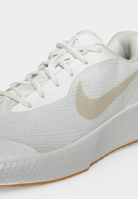 Λευκό αθλητικό παπούτσι Nike με μπεζ σήμα, λευκά κορδόνια, υφασμάτινο πάνω μέρος με υφή και σόλα σε χρώμα τσίχλας.