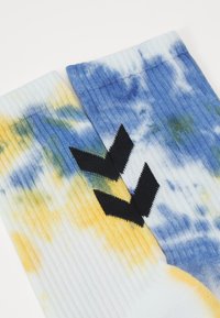 Šarene sokne s uzorkom tie-dye u plavim, žutim i zelenim nijansama, s rebrastom teksturom i crnim chevron logotipom.