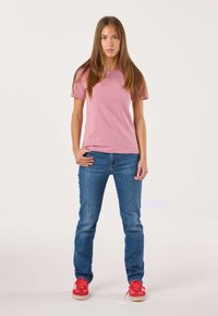 Maglietta rosa chiaro in cotone abbinata a jeans in denim blu e sneakers rosse. La vestibilità è casual, con maniche corte e una forma classica.