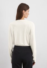 Vit långärmad topp gjord av mjukt material, med rund halsringning och avslappnad passform, i kombination med mörka skräddarsydda byxor.