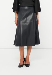 Jupe midi en cuir noir avec un ourlet évasé, dotée de détails de panneaux cousus, associée à des chaussures à talons hauts noires.