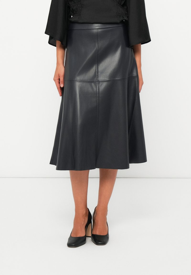 Jupe midi en cuir noir avec un ourlet évasé, dotée de détails de panneaux cousus, associée à des chaussures à talons hauts noires.