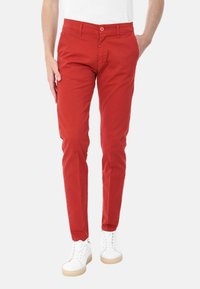 Pantaloni di cotone rossi con una vestibilità slim, tasche frontali e chiusura con un singolo bottone. Abbinati a sneakers bianche e a una camicia bianca semplice.