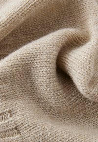 Tissu tricoté beige avec une texture douce, présentant un motif de points régulier et des variations subtiles d'épaisseur.