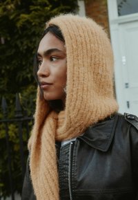 Hellorange gestrickter Schal mit weicher, flauschiger Textur, um den Hals drapiert, kombiniert mit einer schwarzen Lederjacke mit Reißverschluss.