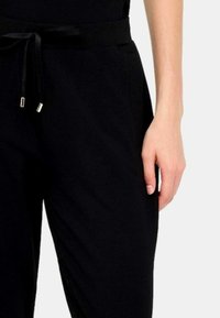 Pantaloni neri realizzati in tessuto morbido, con vita regolabile, silhouette elegante e sottili dettagli in oro.