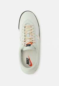 Ανοιχτό πράσινο αθλητικ ό παπούτσι με ομαλή υφή, μπεζ κορδόνια, μαύρη καουτσούκ σόλα και έντονο πορτοκαλί λογότυπο Nike στη γλώσσα.