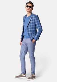 Niebieska marynarka w kratę, niebieski sweter, jasnoniebieskie spodnie i szare trampki. Gładki materiał, dopasowany krój i okulary przeciwsłoneczne. Luzacki, skoordynowany wygląd.