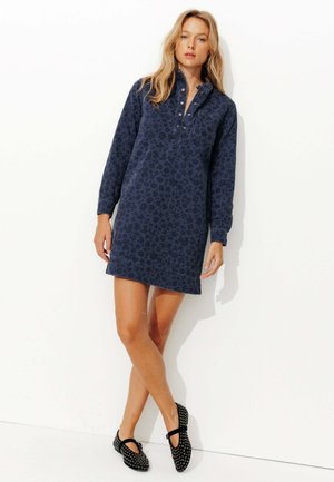 Robe bleu marine avec imprimé léopard, manches longues et col avec boutons. Associée à des chaussures noires avec des accents cloutés.