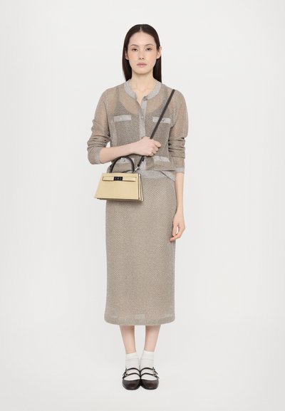 Beige strikket cardigan over en matchende knælang kjole, parret med en gul struktureret håndtaske og mørke sko, med hvide sokker.