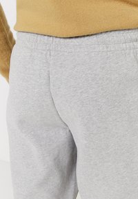 Grijze joggingbroek van zachte stof, met een elastische tailleband en een gladde textuur. Het zichtbare detail toont de achterkant van de broek.
