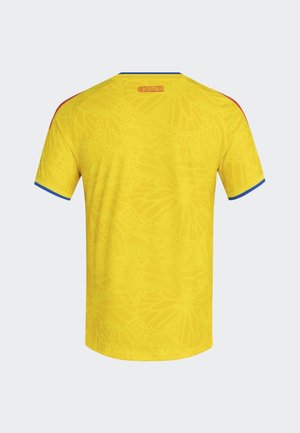 Jersey amarillo con un sutil patrón de mariposas, acentos azules en las mangas y el texto "COLOMBIA" bordado en el cuello trasero.