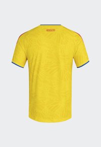 Maillot jaune présentant un motif de papillons subtil, des accents bleus sur les manches et le texte "COLOMBIE" brodé sur le col derrière.