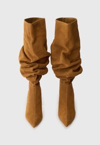 Bottes en daim marron jusqu'au genou avec un design flou, un bout pointu et une texture lisse. Présente un haut repliable pour un détail supplémentaire.