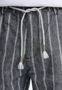 Grå og hvide bukser med lodrette striber og en hvid flettet snøre, der er bundet i en sløjfe i taljen.