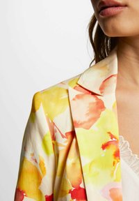 Blazer floral en crema con patrones en acuarela amarillos, naranjas y rojos. Tejido suave, solapas clásicas, corte entallado y hombros estructurados.