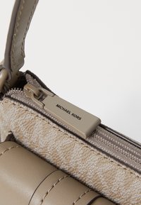 Beige Michael Kors handbag featuring textured fabric, smooth leather accents, a zip closure with branded hardware, and a compact design.