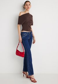 Bruine off-shoulder top, getailleerde taille, blauwe denim flare jeans, rode handtas met een enkele riem en rode sandalen met bandjes en hoge hakken.