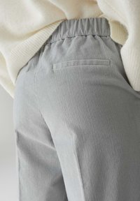 Pantaloni in velluto a coste grigi con una finitura testurizzata, vita elastica e tasca posteriore, abbinati a un top tricot crema parzialmente visibile.