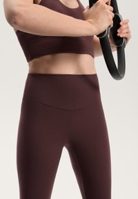 Bordo športni modrček in hlače z visokim pasom, oboje izdelano iz gladkega, elastičnega materiala. Modrček ima zaobljen izrez in brezšivno zasnovo.