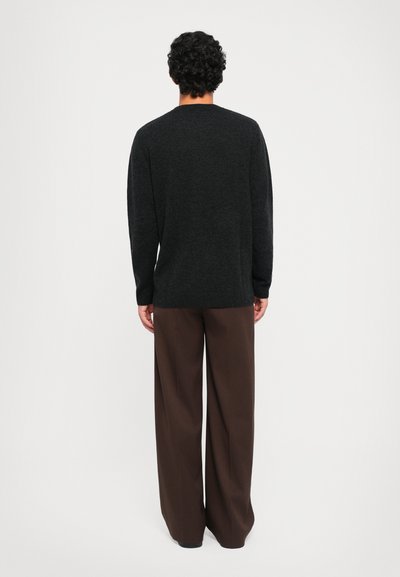 Dunkelgrauer Langarmpullover mit Rundhals, kombiniert mit lockeren braunen Hosen. Geschmeidige Textur und gerippte Saumdetails sind sichtbar.