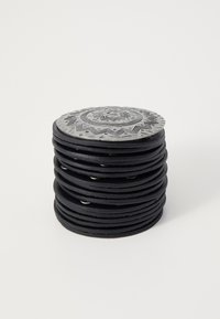 Melnas apļa formas trauku kaudze, ar dekoratīvu metāla virsmu, kas rotāta ar sarežģītiem rakstiem un tekstūrām, kontrastējot ar gludu pamatni.