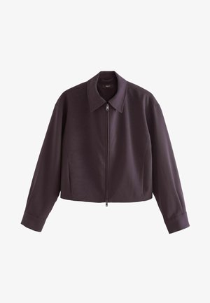 Skrócona kurtka z ciemnofioletowego materiału, z zaostrzonym kołnierzem, pełnym zamkiem błyskawicznym z przodu oraz długimi rękawami z mankietami zapinanymi na guziki.