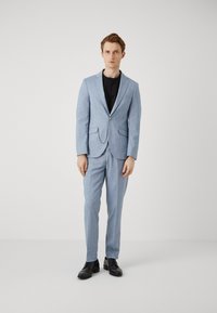 Lichtblauw pak gemaakt van een getextureerde stof, met een enkele knoopsluiting, notch revers en bijpassende broeken, gecombineerd met zwarte schoenen.