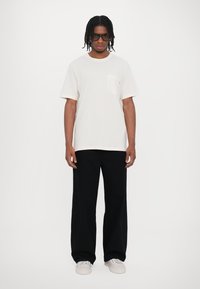 Vit bomull t-shirt med korta ärmar och ficka, som matchas med svarta vida byxor och vita sneakers. Klara solglasögon fulländar looken.