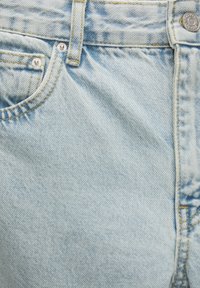 Jeans de mezclilla azul claro con un acabado texturizado, que cuentan con un cierre de botón, dos bolsillos frontales y detalles de costura visibles.