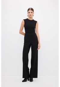 Haut sans manches noir avec une silhouette ajustée, associé à un pantalon noir taille haute à jambes larges, porté avec des bottines à talons noires.