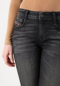 Jeans in denim grigio scuro con un design aderente, dotati di chiusura con bottone, tasche frontali e un dettagliato brandizzato sulla tasca.