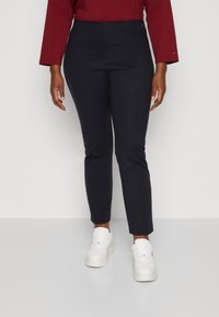 Marina höga byxor med slim-fit design och platt front, kombinerat med vita plattformssneakers. Slät tyg och skräddarsydd form.