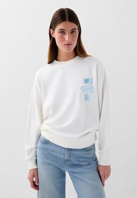 Witte katoenen sweatshirt met een ronde hals, voorzien van lichtblauwe graphic designs op de linkerborst, gecombineerd met lichtblauwe spijkerbroek.