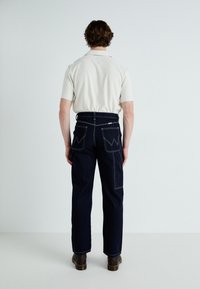 Dark denim jeans with a straight leg fit, featuring contrast stitching and two back pockets with a unique W-shaped design.