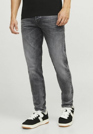 Graue Jeans im Slim-Fit-Stil mit feiner Textur, Fünf-Taschen-Design und abgenutztem Finish, kombiniert mit schwarzen Sneakern mit weißen Akzenten.
