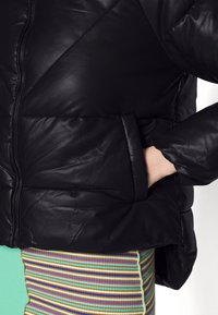 Veste rembourrée noire avec fermeture éclair et détails cousus. Elle possède une poche latérale et est assortie à un vêtement à rayures multicolores.