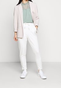 Světlý růžový blazer s texturovanou látkou, mintově zelený top se krajkovým lemem, bílé zúžené kalhoty a bílé tenisky. Zcasualní outfit s čistými liniemi.