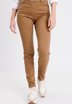 Lichtbruine high-waisted broek gemaakt van zachte katoenmix, met een slim fit ontwerp en voorkantenzakken. Gepaard met beige sneakers.