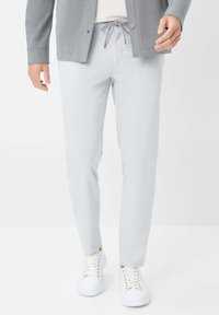Light gray jogger pants with a smooth texture and elastic waistband, featuring a drawstring and slim fit, paired with white sneakers.